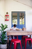 Boy at a rustic wooden table with red classic stools and green plants