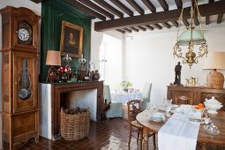 Porcelain crockery on wooden table and antique long-case clock next to open fireplace in dining room