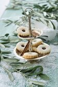 Jam sandwich biscuits on a cake stand between olives sprigs on a table covered with snow