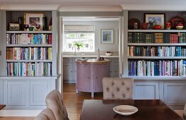 View from dining room with bookcases into rustic kitchen with pastel panelled cabinets