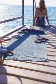 Woman sitting on jetty next to beach towel and denim bag