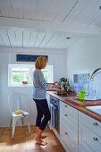 Woman in bright country-house kitchen with wood-beamed ceiling