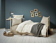 Vintage-style metal bed with pillows and blankets in natural shades against blue-grey wall