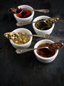 Vier Vintage-Löffel mit verschiedenen Teesorten auf Teeschalen