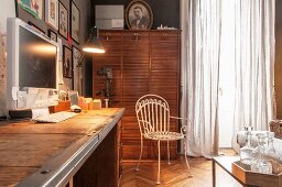 Lamp in front of computer on desk, white metal chair and antique filing cabinet with roller doors
