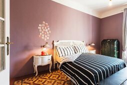 Schlafzimmer mit antikem Bett und schwarz-weiss gestreifter Bettwäsche, Fotodekoration an mauvefarbener Wand