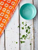 A blue bowl on a white shabby wooden table with a bright orange napkin and chopped parsley