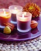 Lit scented candles on purple plate decorated with physalis husks