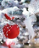 Red bauble and pair of bird ornaments on white-sprayed branches of Christmas tree