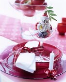Festive place setting with red glass dishes embellished with Christmas tree decorations