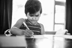 Kleiner Junge schreibt auf Blatt Papier (s/w-Foto)
