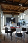 Modern, open-plan kitchen below rustic wood-beamed ceiling
