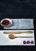 Schokoladenkonfekt auf Marmorbrett mit Besteck, Cranberries im Schälchen auf Tuch