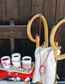 weiße, dekorierte Porzellanbecher mit Glühwein und Holzschlitten vor rustikaler Hütte