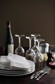 Tellerstapel, Stoffservietten, Weingläser, Weinflasche und Gewürze auf Holztisch