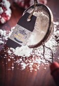 A sieve with icing sugar and a Christmas gift tag