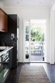 Black fitted kitchen in an old building with an open, white patio door