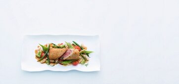 Saddle of lamb wrapped in white bread on a bed of mixed beans