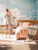 Doppelbett vor Studiowand mit Himmelmotiv, Frau im Hintergrund