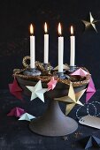 A unique Advent wreath on a cake stand decorated with paper stars, a golden garland and four burning candles