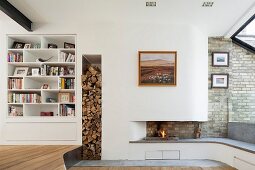 Open fire in modern fireplace with integrated fireplace bench and firewood stacked in vertical niche next to white fitted shelves