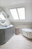 Free-standing bathtub and grey country-style washstand in bathroom in converted attic