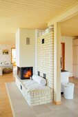 Cosy seating area in front of fire in brick partition wall in open-plan interior with pale wooden ceiling