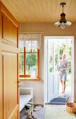 Hausflur mit Holzbank vor Sprossenfenster und Frau in offener Haustür