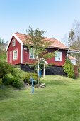 Blick auf rotbraunes Schwedenhaus mit weissen Fenstern unter blauem Himmel