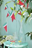 Glass carafe on metal chair below hand-made bunting on wooden fence
