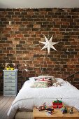 Bed below star-shaped lamp on rustic brick wall in boy's bedroom