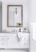 White vanity with marble top and wall mirror on tiled wall