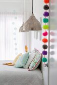 Bunte Pompon-Girlande an Zimmertür in hellem Schlafzimmer mit Pendelleuchten und pastellfarbenen Kissen