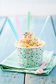 Vanilla ice cream with coloured sugar sprinkles in a paper ice cream tub with spoons