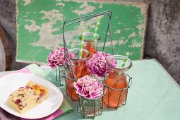 Carafes of rhubarb juice and carnations in drinking glasses in bottle carrier