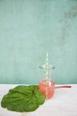 Drinking straw in carafe of rhubarb juice next to wrapped in rhubarb leaf
