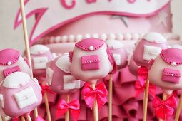 Pink cake pops shaped like schoolbags with a pink cake in the background