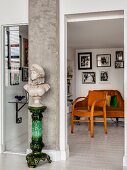 Bust on green plinth against concrete pillar in front of vintage armchair and sofa in reading area