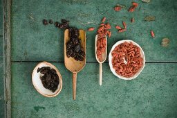 Dried cranberries and goji berries in wooden scoops and bowls on a rustic wooden surface