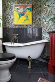 Free-standing clawfoot bathtub, black splashback on wall and modern artwork on floral wallpaper in vintage-style bathroom