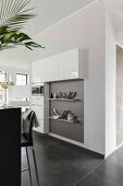 A made-to-measure kitchen cupboard partially built in to a wall with wall shelves in an open plan kitchen