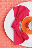 Knotted linen napkin and orange cup on white plate