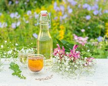 Selbstgemachtes Kräuteröl und Blumen auf Gartentisch