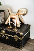 Goldfarbene Hunderfigur und Kerzen auf antikem Mini-Koffer mit Messingverschluss