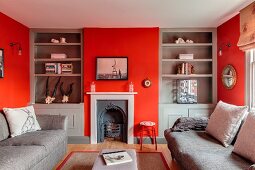 Wohnzimmer mit roten Wänden, grauen Einbauregalen und nostalgischem Kamin
