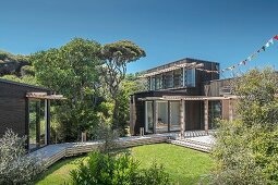 Blick von Garten auf Holzterrasse mit Pergola, vor modernem Wohnhaus