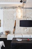 Black lampshade above perforated sheet metal table in loft apartment with brick wall