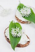 Brotscheibe belegt mit Frischkäse, Bärlauchblättern und essbaren Bärlauchblüten