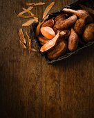Sweet potatoes in a rustic wooden basket and peelings on a wooden table