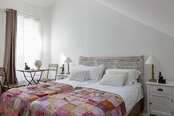 Double bed with headboard, patchwork bedspread, vintage garden table and folding chairs next to window